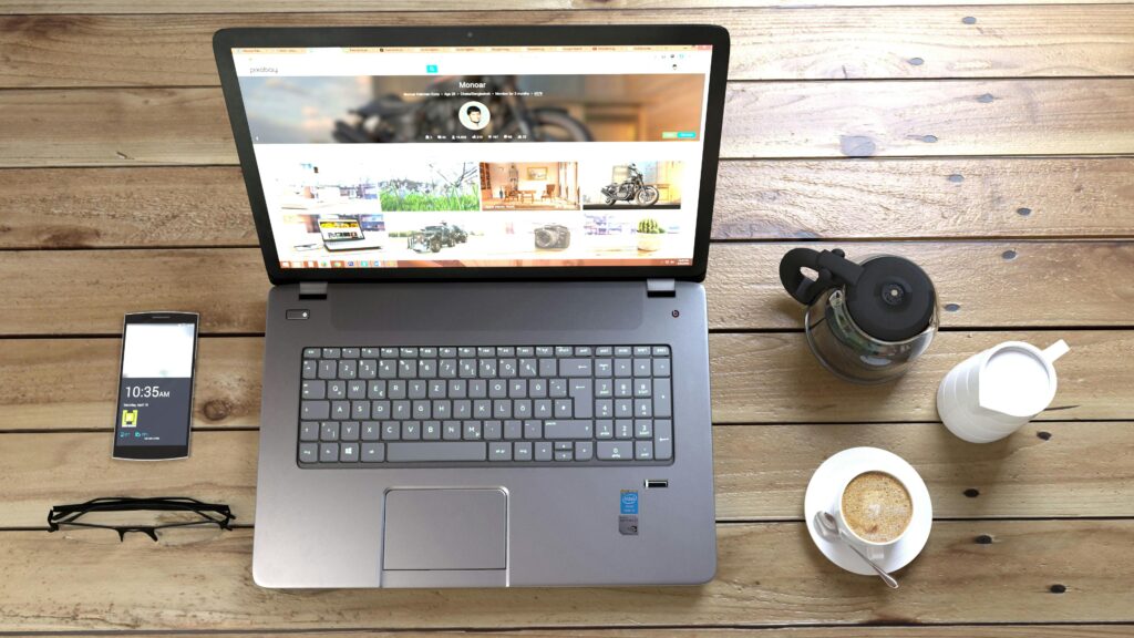 Top view of a laptop, smartphone, coffee, and glasses on a wooden desk.